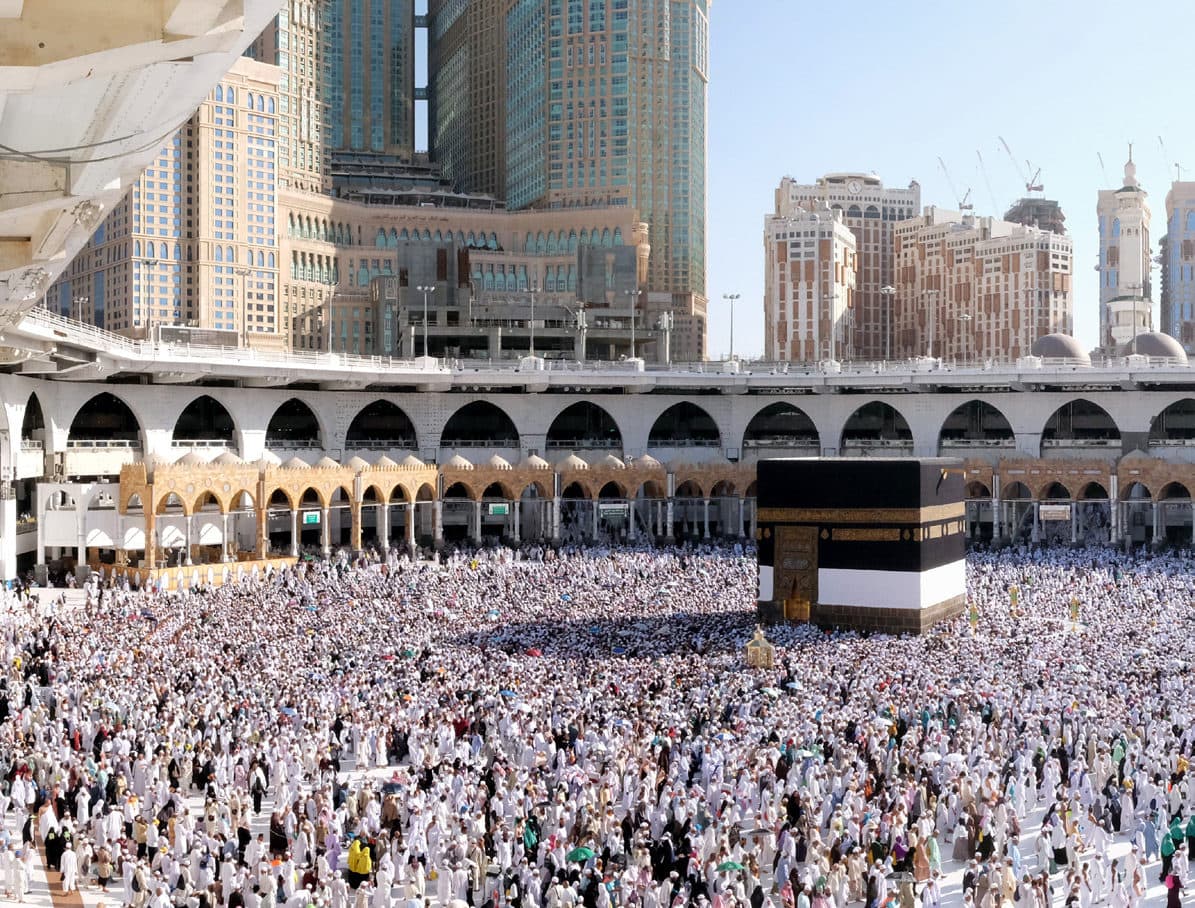 حجاج بلباس أبيض يملؤون صحن الطواف حول الكعبة المشرفة، وخلفهم أروقة المسجد الحرام وأبراج مكة المكرمة